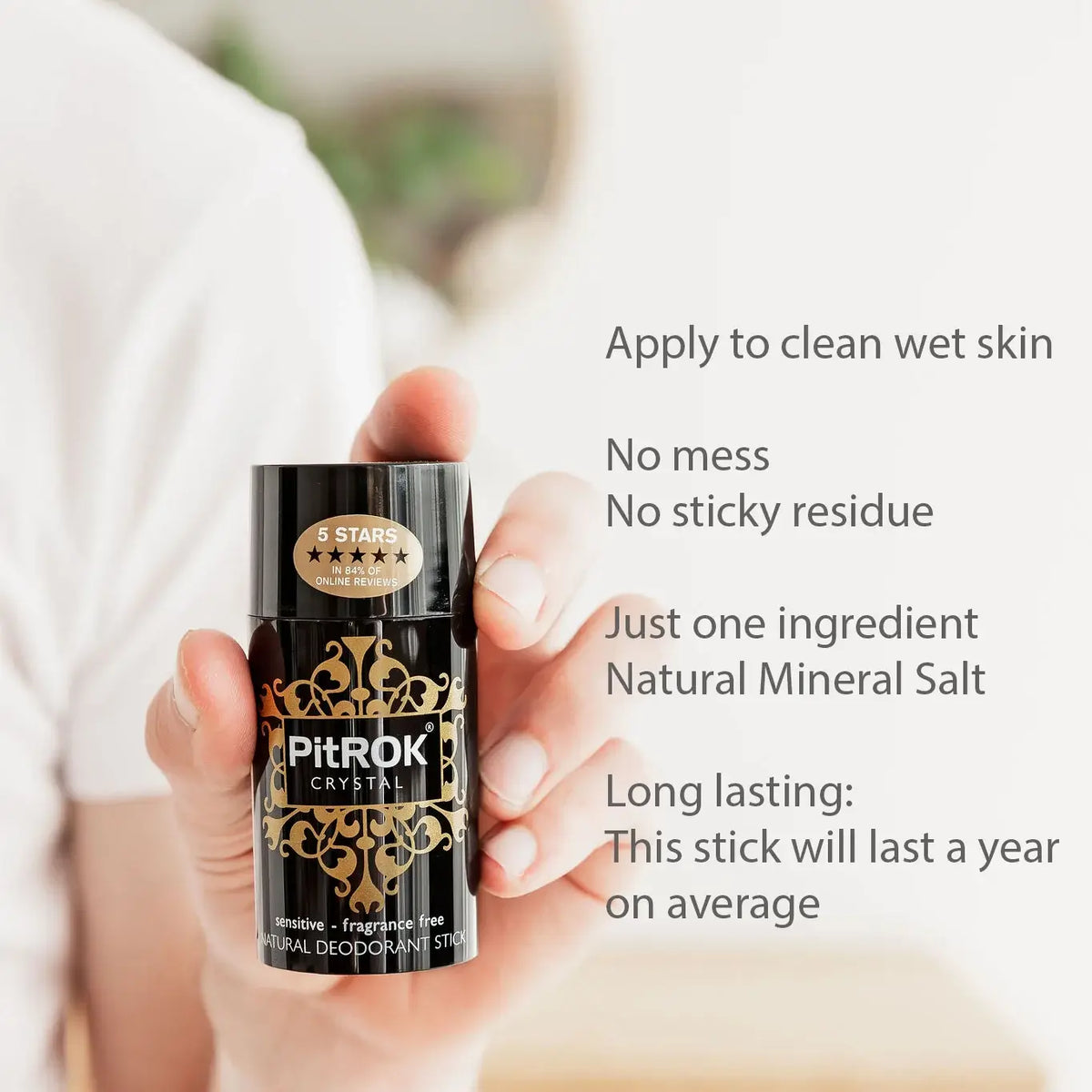 A hand holding a black and gold PitROK Crystal sensitive deodorant stick, with promotional text on the right detailing its benefits.
