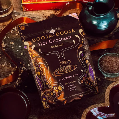 Booja Booja Hot Chocolate Organic packaging displayed on a wooden surface with ingredients and a pot.