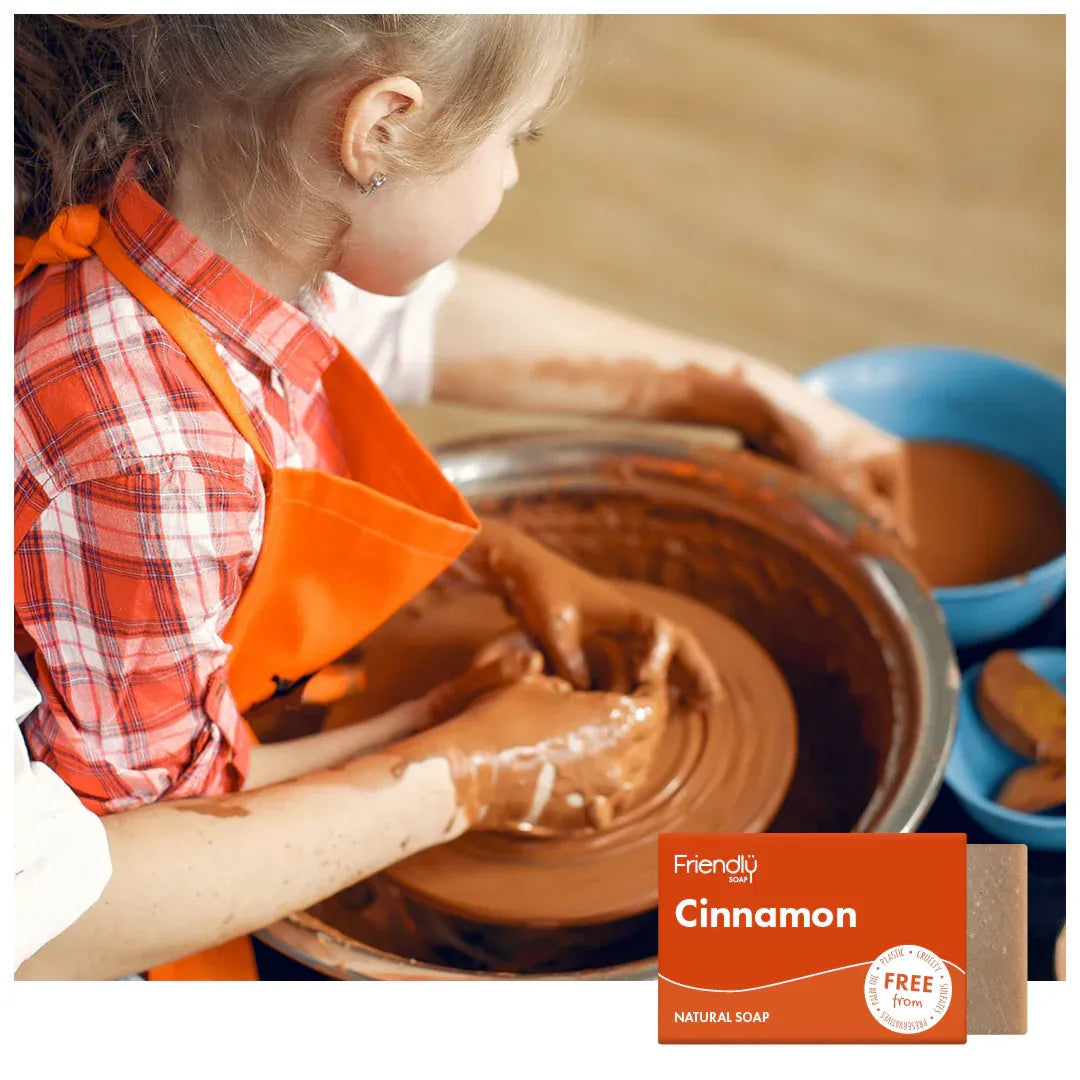 Child in an orange apron working with clay on a pottery wheel, with Friendly Soap cinnamon bar in the corner.