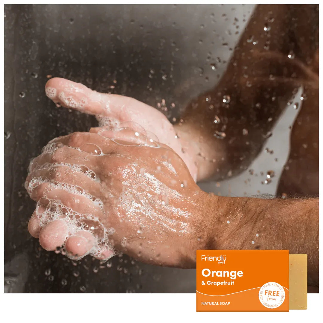 Person washing hands with soap, displaying a bar of soap labeled 'Orange & Grapefruit' from Friendly Soap.