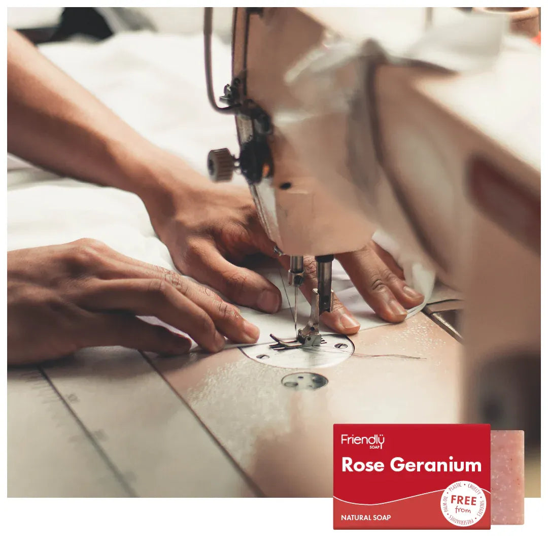 Person using a sewing machine with a 'Friendly Soap' rose geranium soap bar in the foreground.