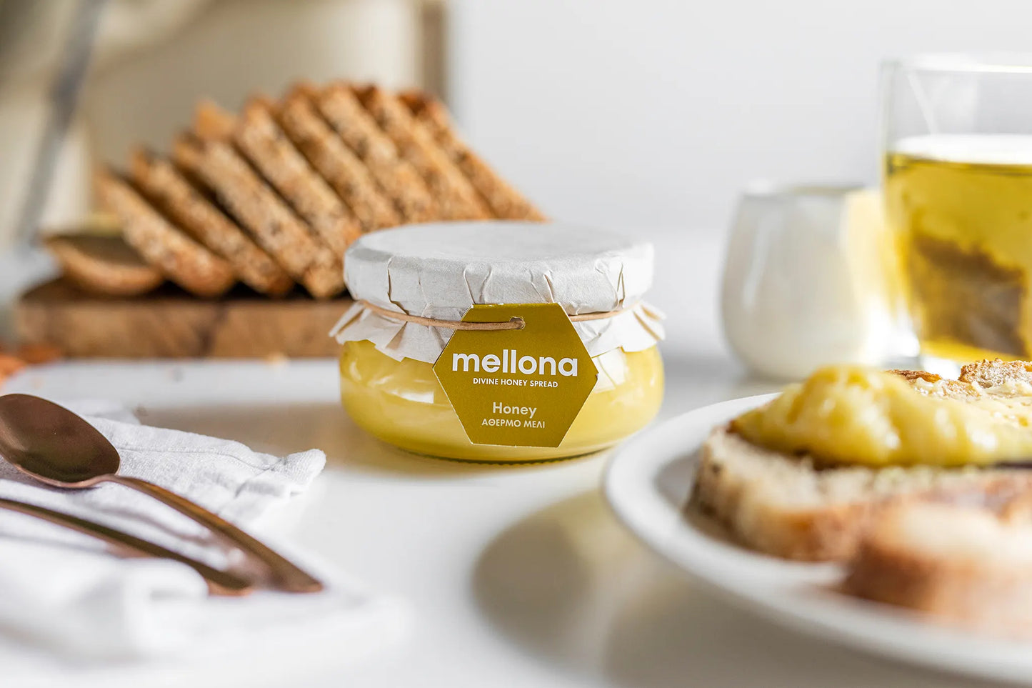 Mellona Raw Honey 230g jar placed on a table with bread and honey, showcasing pure, natural sweetness.